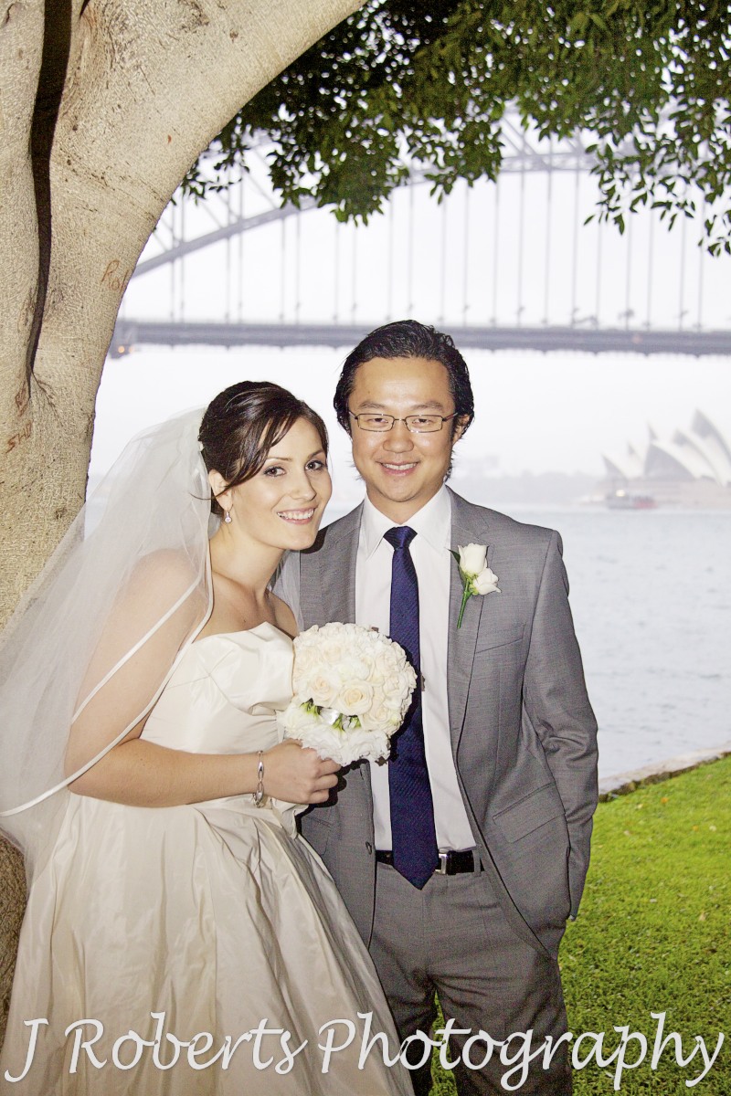 Bride and groom portrait under tree with Sydney Harbour Bridge and Opera House in the background - wedding photography sydney